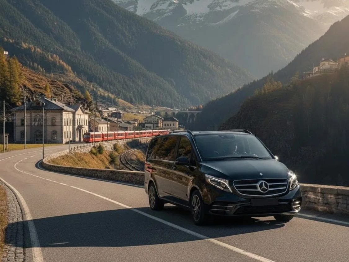 Minivan Mercedes nero su una strada di montagna vicino a una stazione con un treno rosso