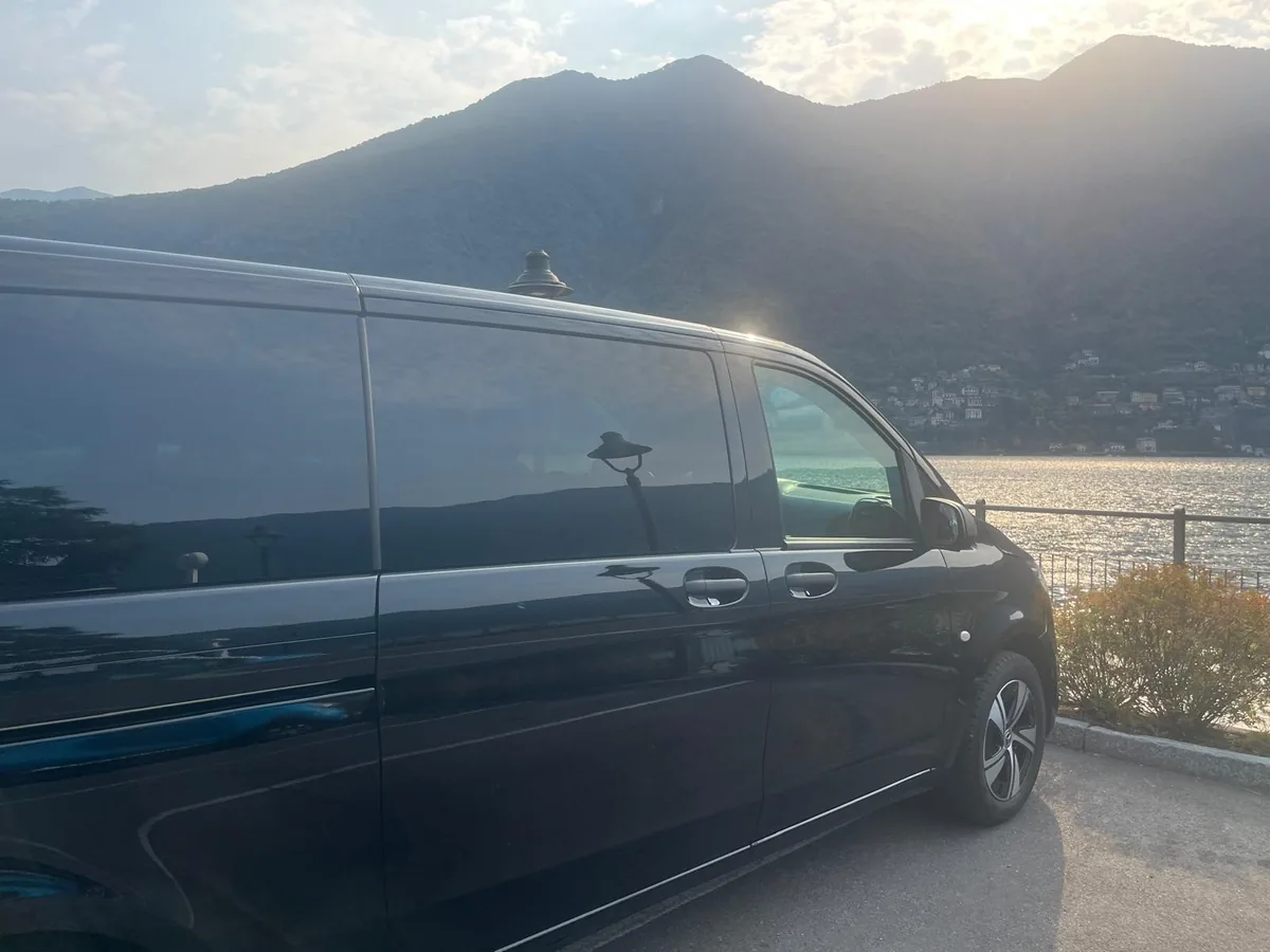 Black Mercedes minivan by the lake at sunset, with the mountains behind