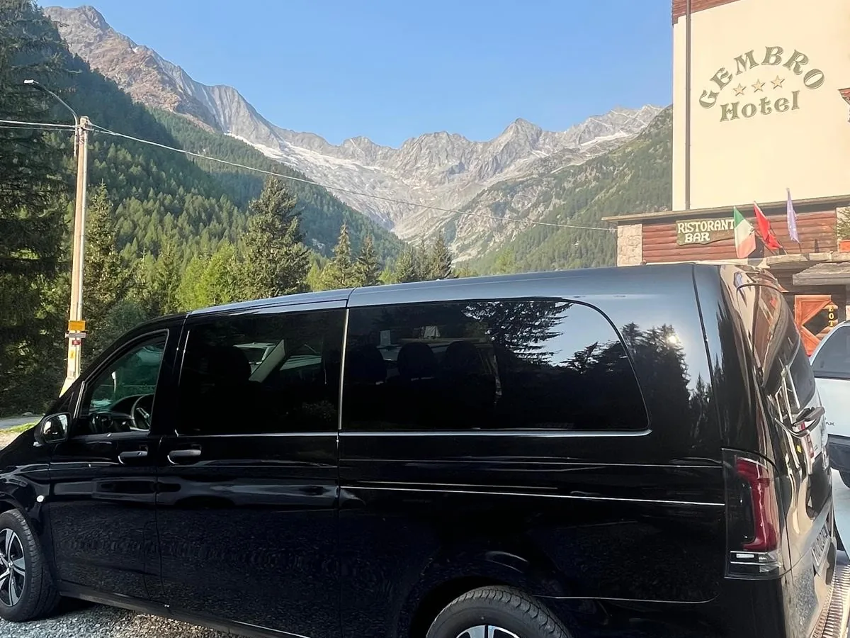 Black Mercedes minivan outside a mountain hotel, with glaciers behind